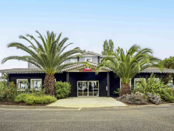 Devanture du Greet hôtel La Teste Bassin d'Arcachon, entourée de verdure et sous un beau ciel bleu